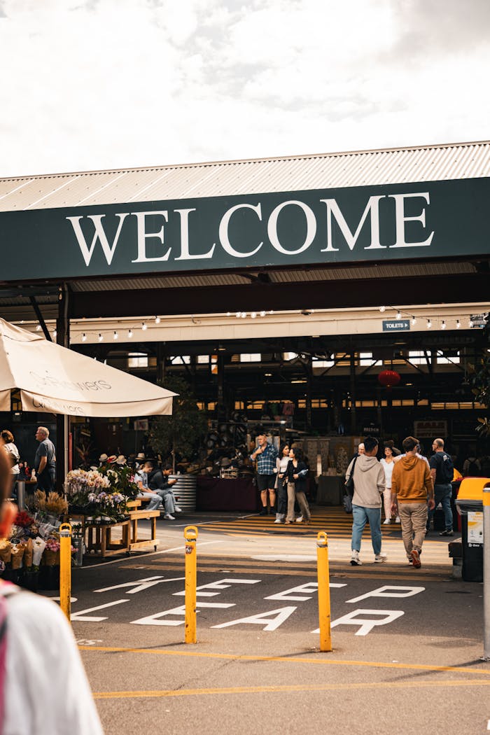 Crowd enters bustling Melbourne market under 'Welcome' sign, capturing vibrant atmosphere.
