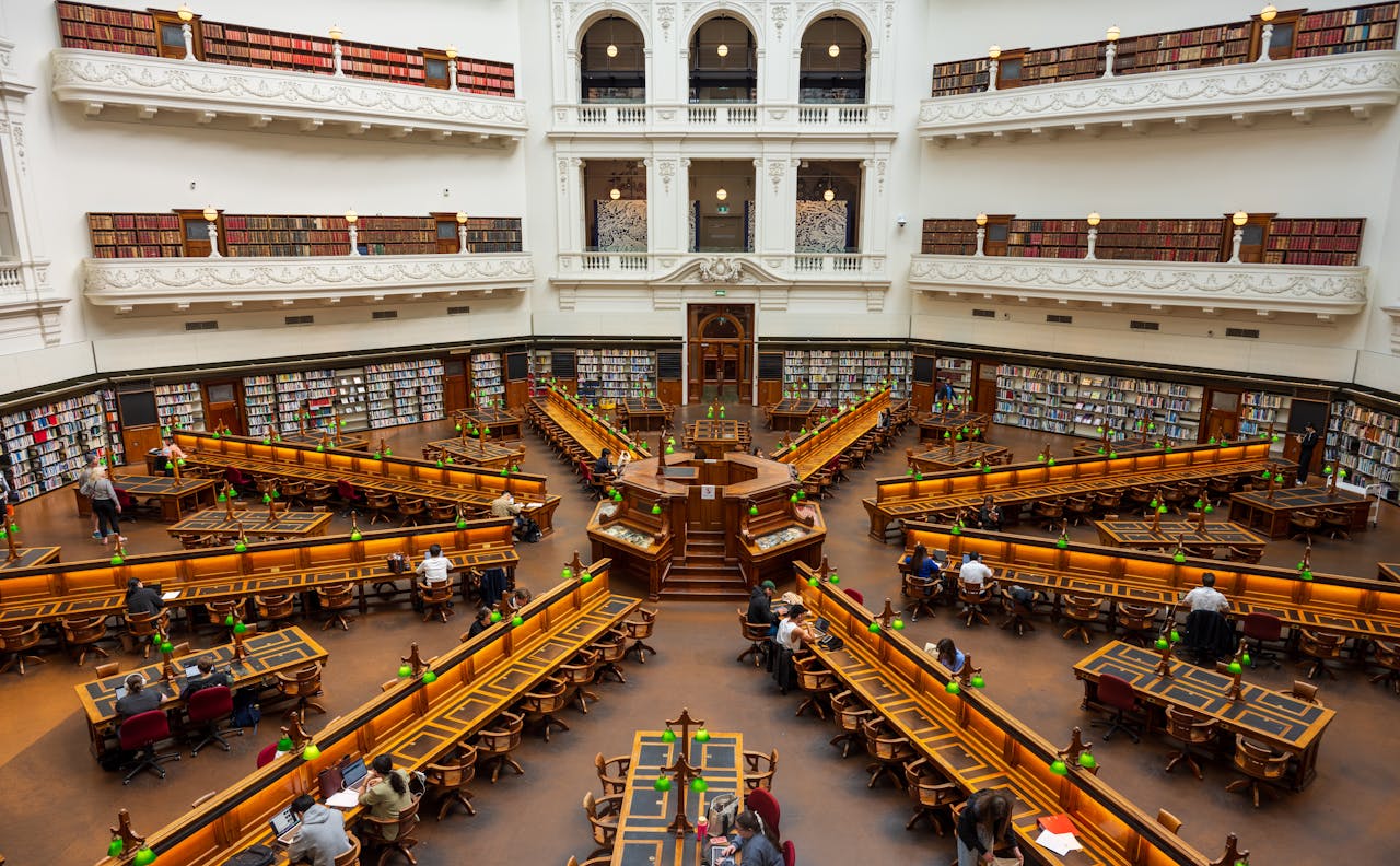 gallery-6 A detailed interior view of a grand library with elegant architecture and people reading.