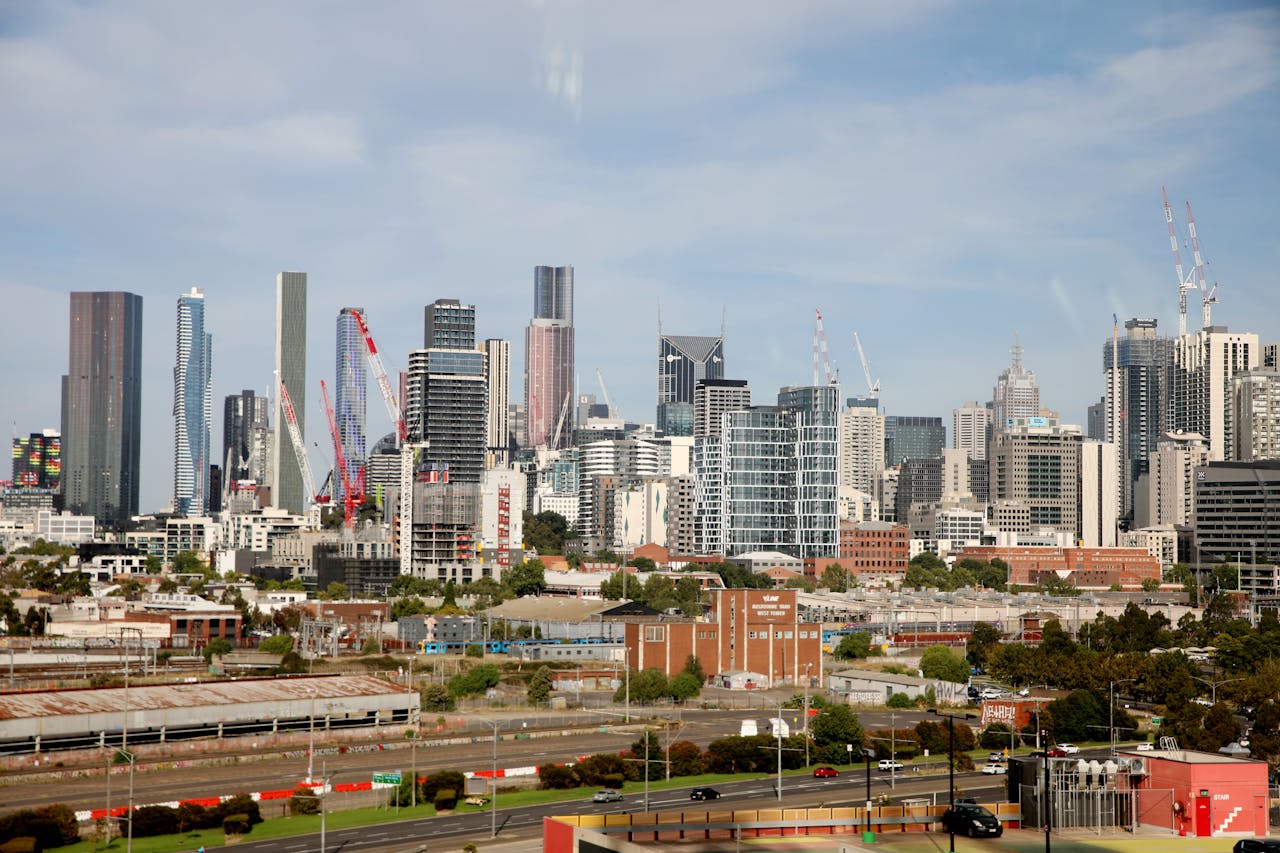 hero-img-01 View of Melbourne's skyline featuring tall skyscrapers and construction cranes under a clear sky.