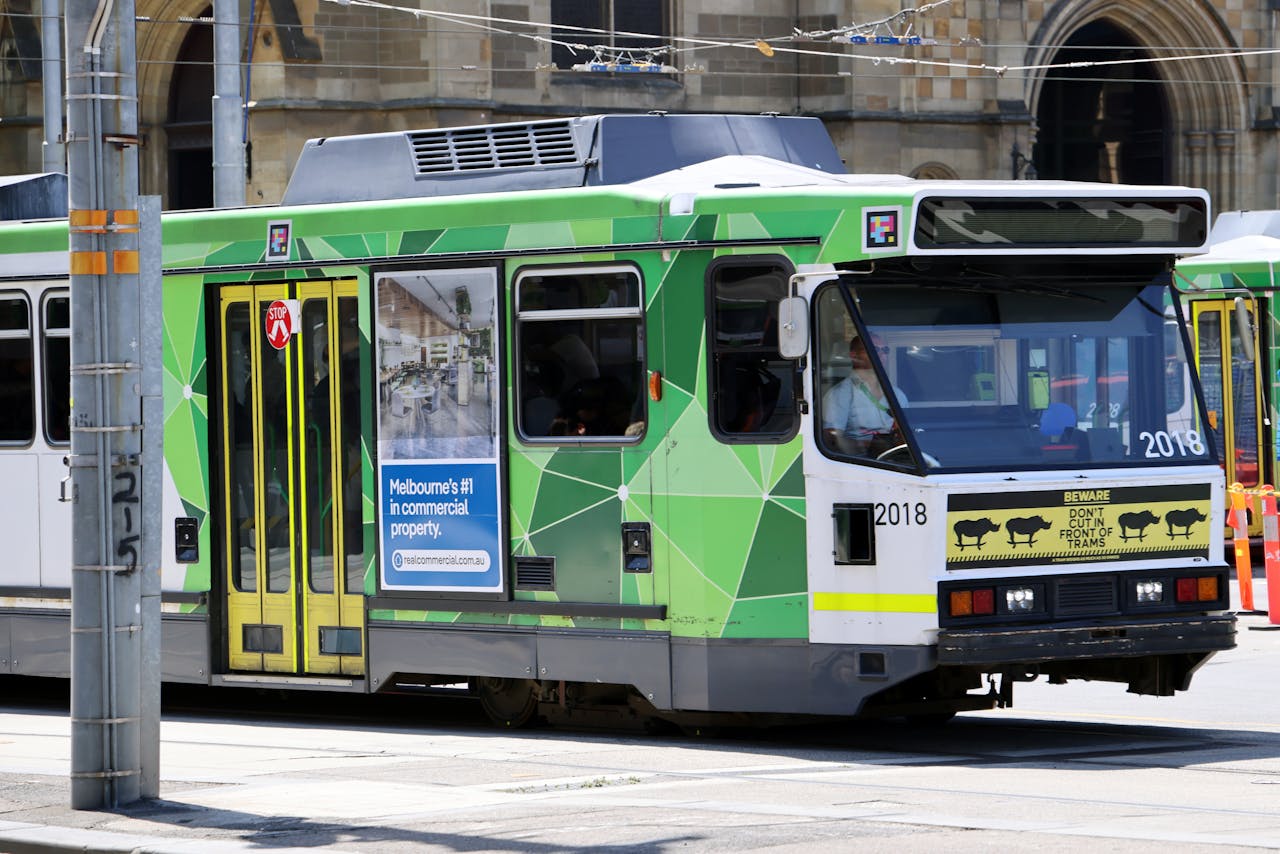 A classic Melbourne tram in vibrant green traversing the city streets against an urban backdrop.